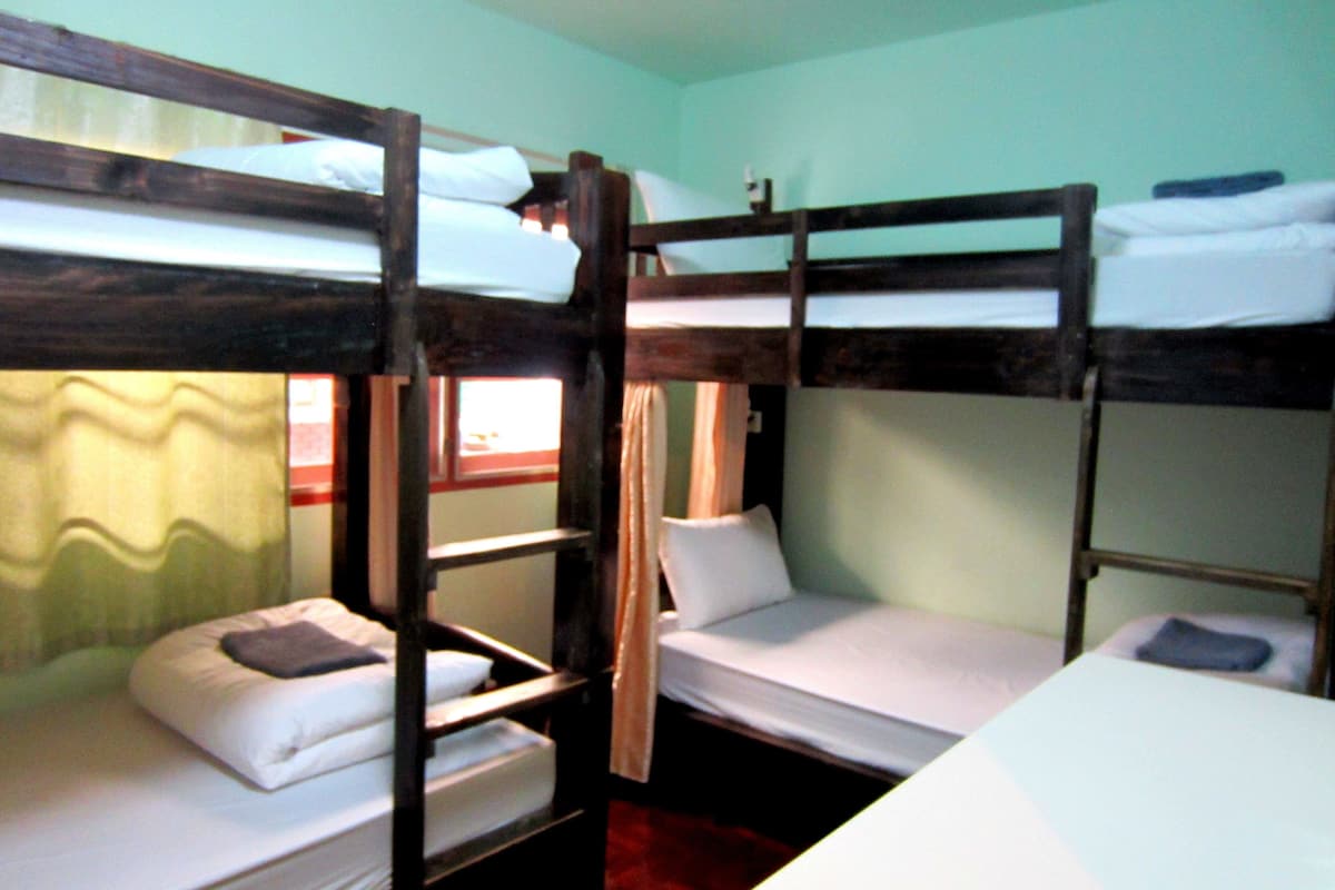 Une chambre avec un lit superposé, deux lits, une fenêtre avec des rideaux et une tête de lit en bois.