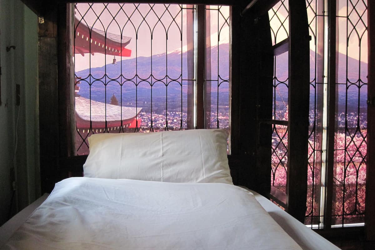 Un lit dans une chambre donnant sur un paysage urbain, visible à travers une fenêtre ornée de barreaux en métal.