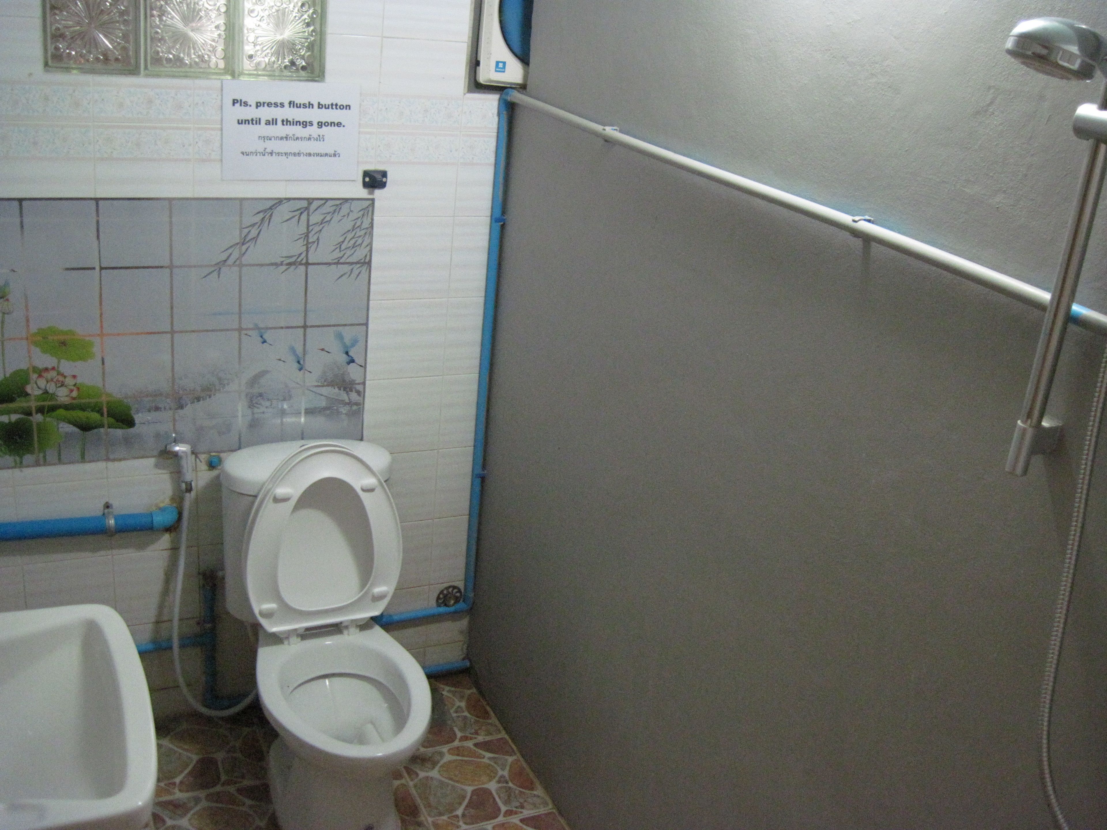 A bathroom with a toilet, bidet, and shower area. There is a sign instructing to press the flush button until all things are gone.