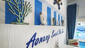 A reception desk with a sign reading "FONANG Sweet Blue Sea" and decorative items including a coral sculpture and a ship figure. - Aonang Sweet Blue Sea (Krabi)