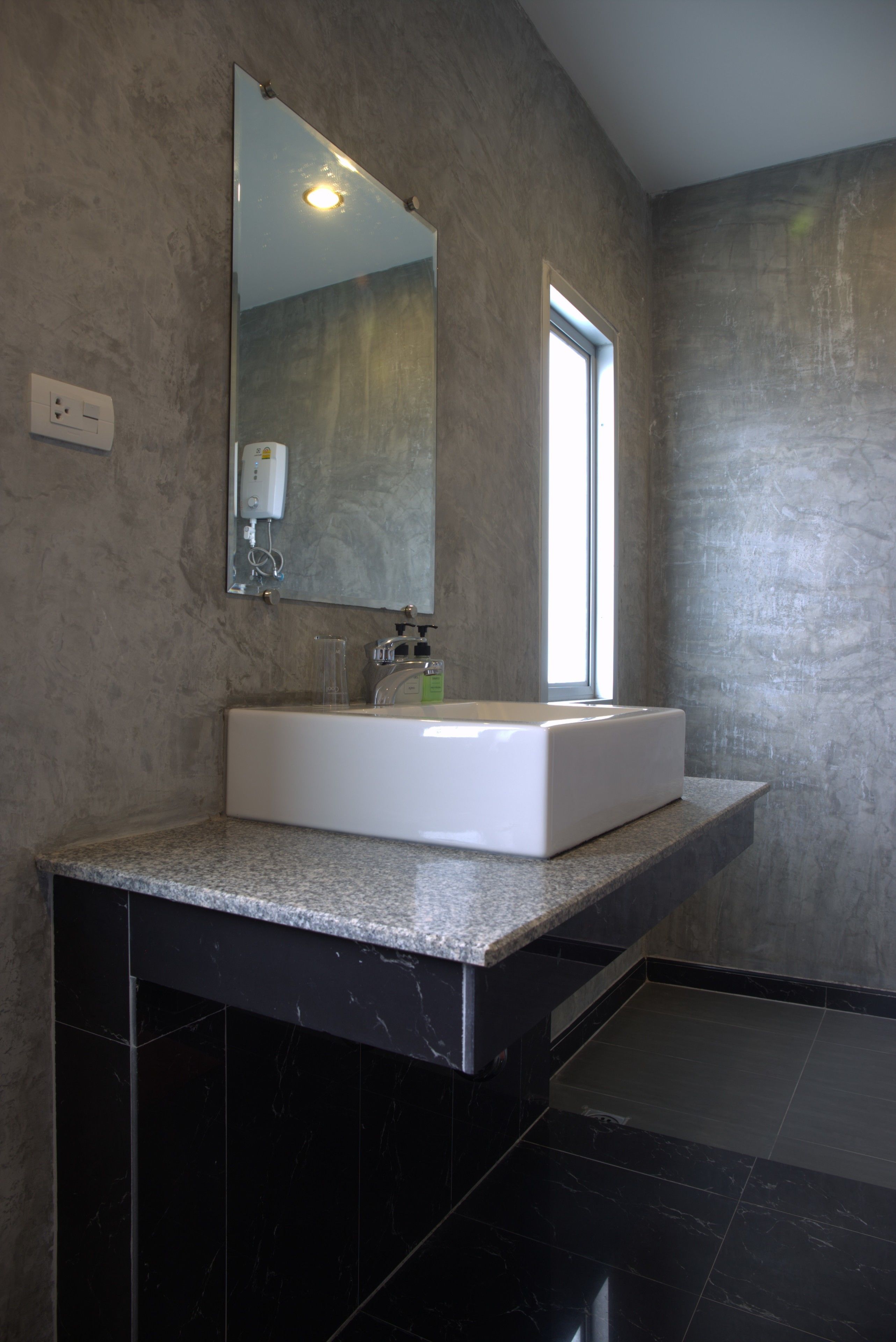 A modern bathroom with a large rectangular sink, a mirror above it, and a window providing natural light.