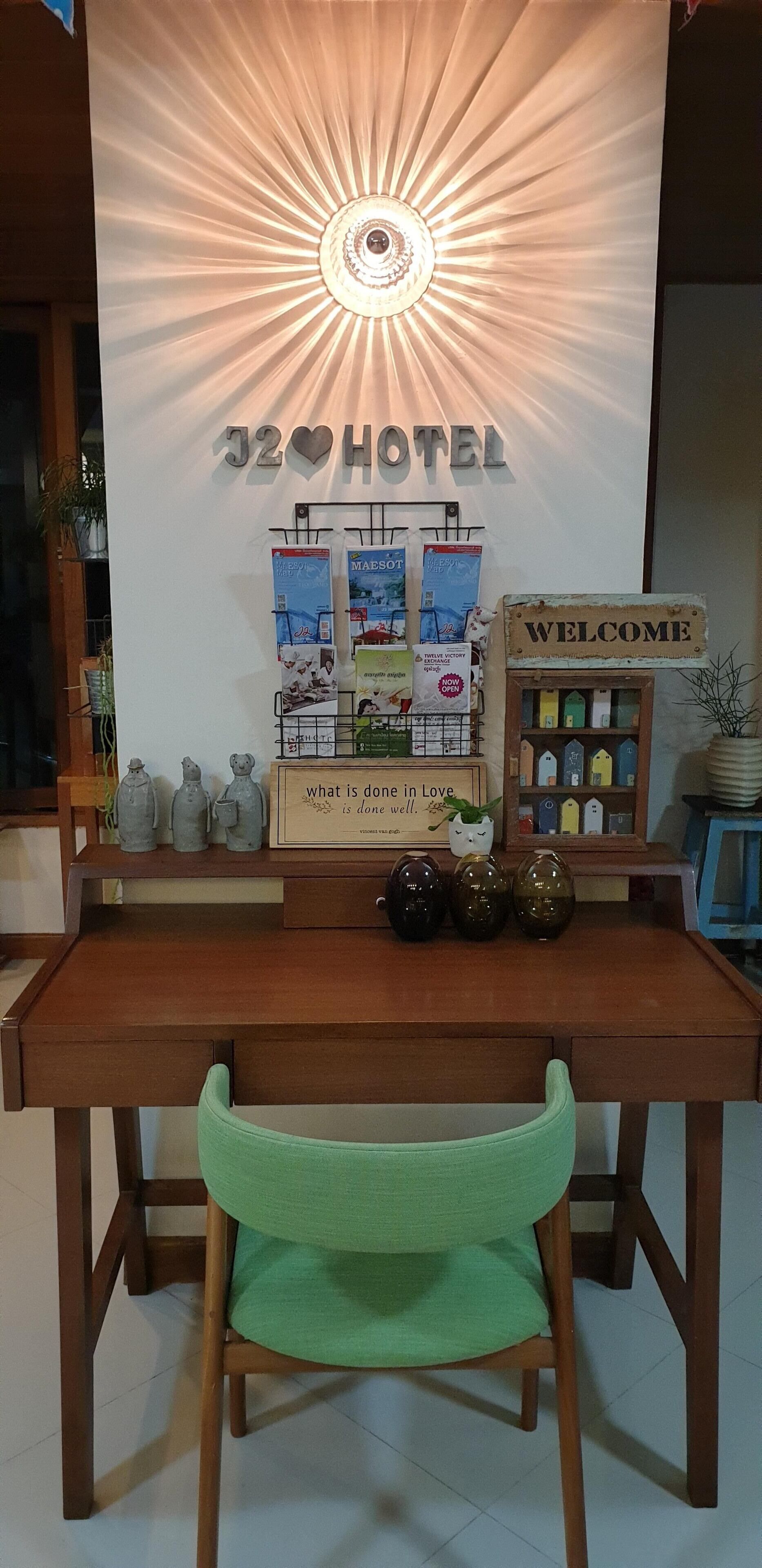 A reception desk with a 'J2 HOTEL' sign, a 'WELCOME' sign, and various promotional materials.