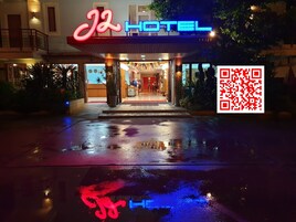 Entrada de hotel con un letrero de neón, pavimento mojado y un código QR.
