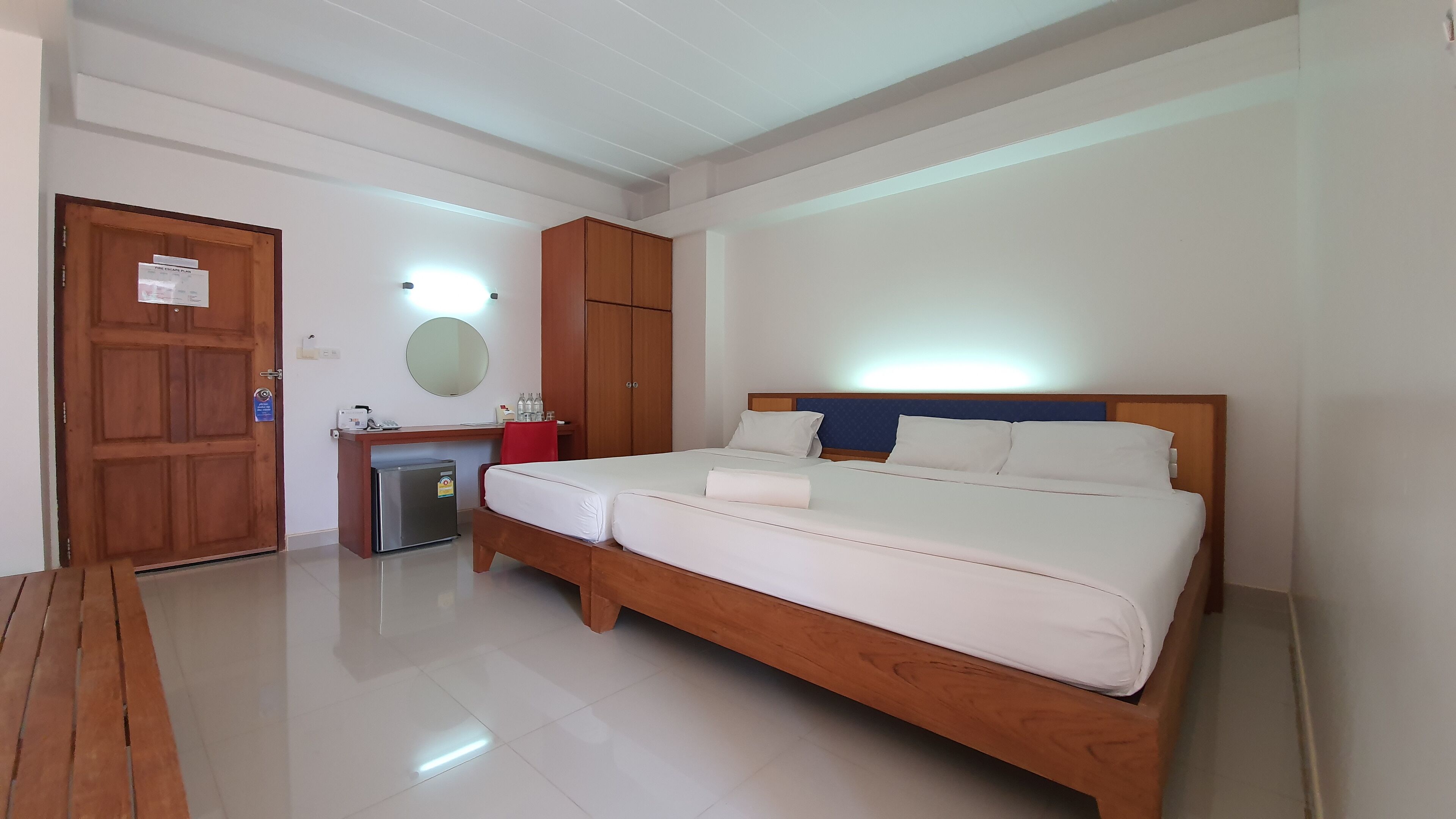 A hotel room with a large bed, a desk with a computer, a small fridge, a mirror, and a wooden door.