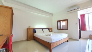 Una cama bien hecha con sábanas blancas, cabecera de madera y una mesita de noche con toallas enrolladas.