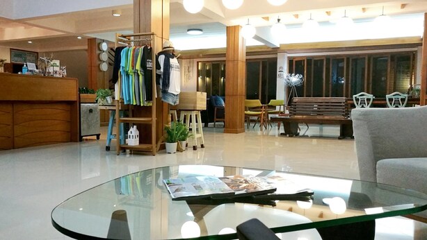 Un moderno vestíbulo de hotel con un mostrador de recepción, un perchero, zonas de estar y una mesa baja de vidrio.