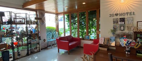 Un hall de hotel con un sofá rojo, techo de madera y una pared con el cartel 'J2 Hotel'.