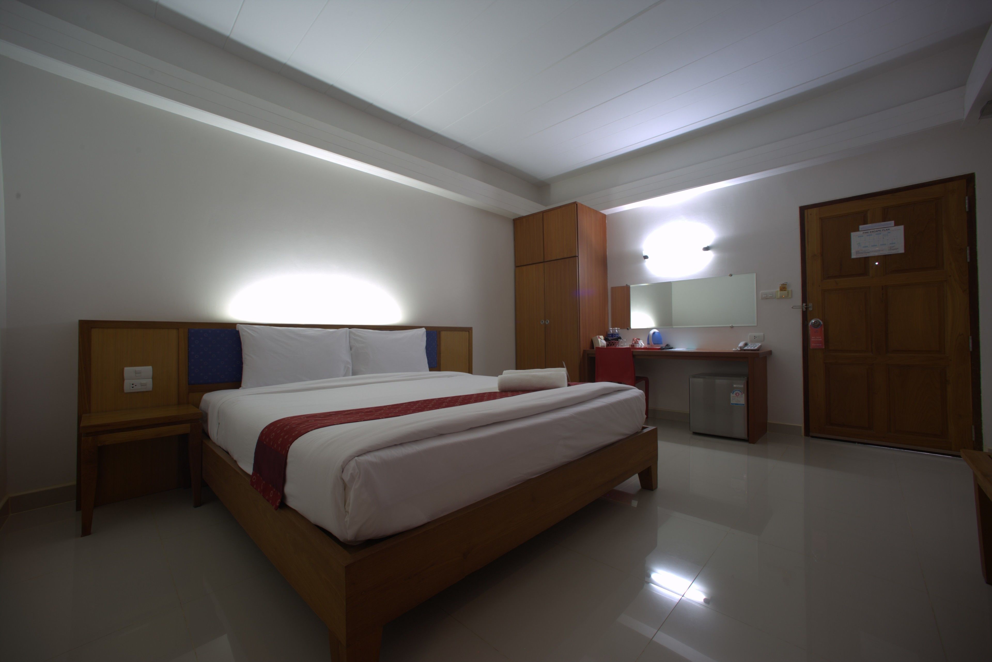 A hotel room with a large bed, a desk, a mirror, and a wardrobe.