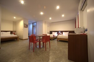 Habitación de hotel con dos camas individuales, una mesa de comedor con sillas rojas, una pequeña cocina y un ventanal grande.