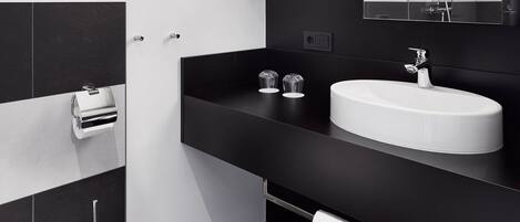 Un baño moderno con un lavamanos blanco, encimera negra y un espejo grande. Hay dos toallas colgadas en la pared y un inodoro con bidé.