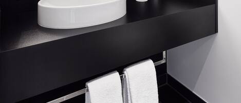 Un baño moderno con encimera negra, lavabo blanco, espejo grande y toallero.