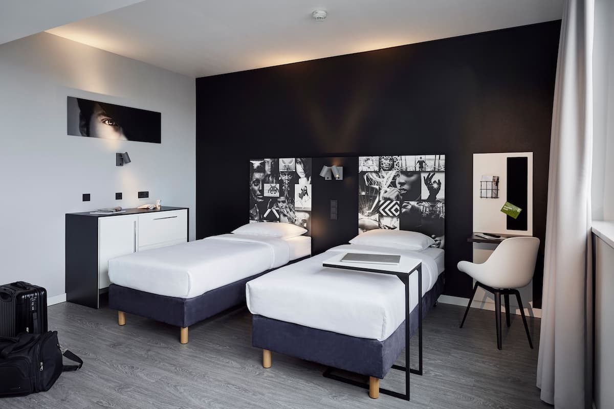 Habitació d'hotel moderna amb dos llits individuals, escriptori, cadira i una gran obra d'art penjada a la paret.