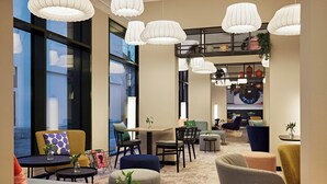 A modern lounge area with multiple seating options, including sofas and chairs, arranged around tables. There are large windows providing natural light and views of the outside. - LEGERE EXPRESS Bielefeld (Bielefeld)