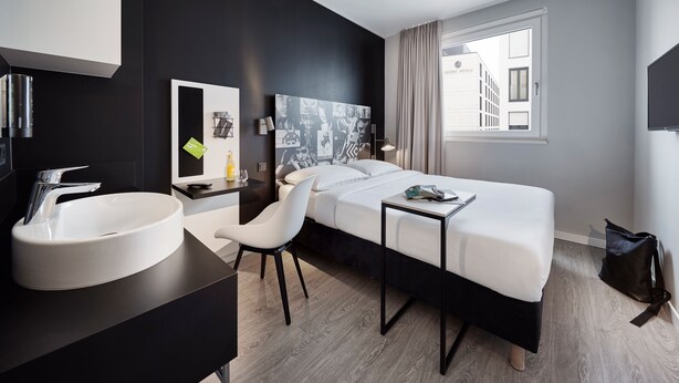 A modern hotel room with a large bed, a round white sink, a desk, and a chair. - LEGERE EXPRESS Bielefeld (Bielefeld)