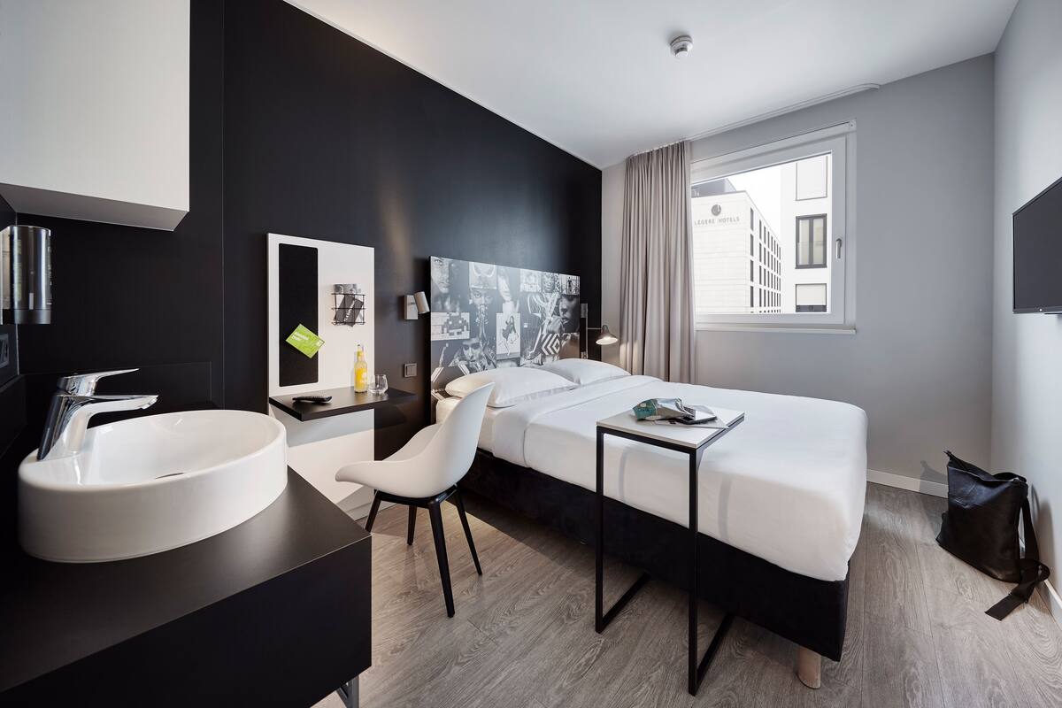Habitació d'hotel moderna amb un llit gran, un lavabo rodó de color blanc, una taula de treball i una cadira.