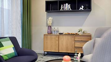 Una sala de estar moderna con un sillón oscuro, un sofá de tonos claros, un mueble de madera con objetos decorativos y una mesa de centro negra.
