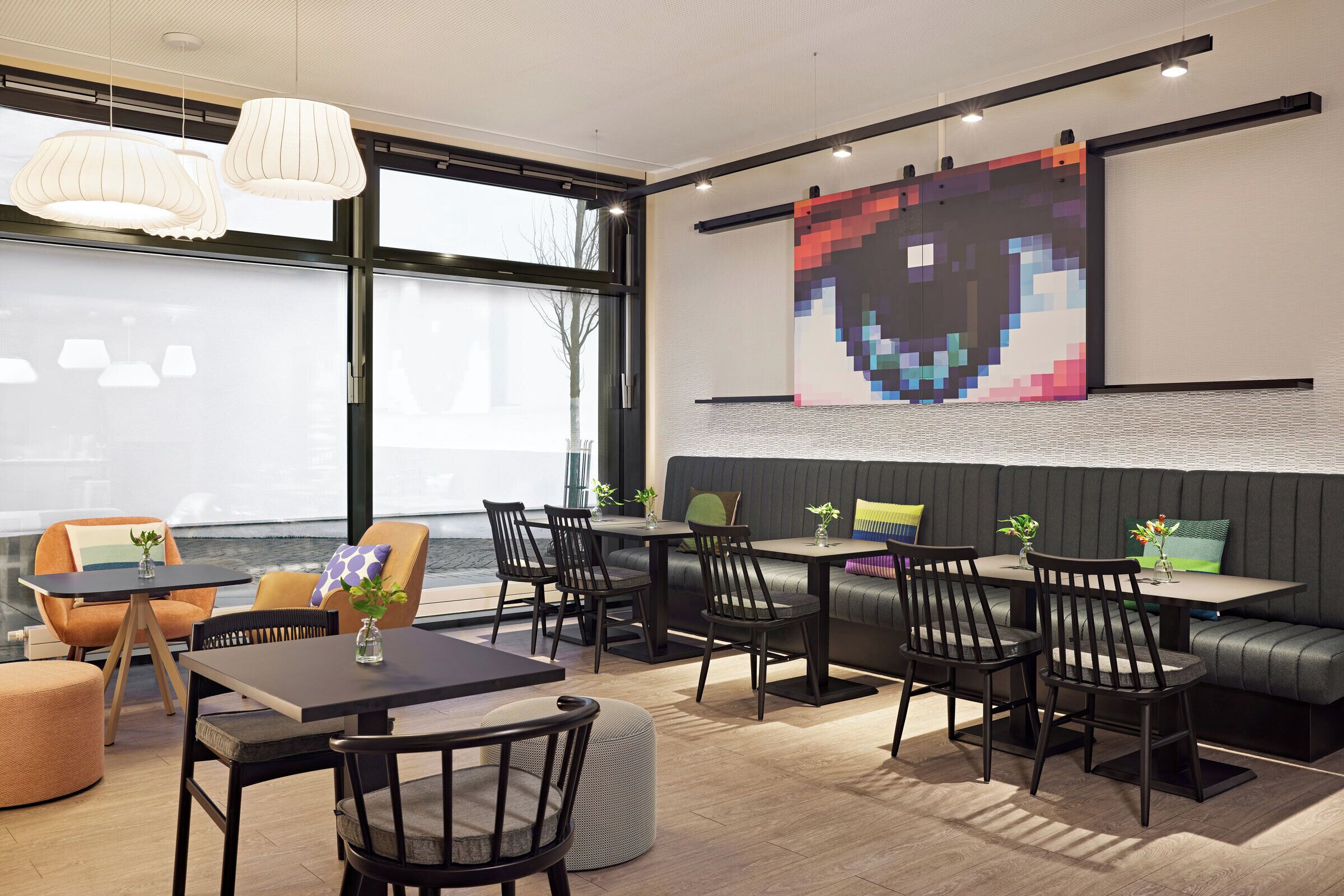 A modern dining area with tables and chairs, a large pixelated artwork on the wall, and a view of the water outside.