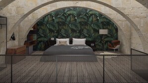 Une chambre à coucher comprenant un lit, une table de chevet, une chaise et un grand mur en pierre en forme d’arc.