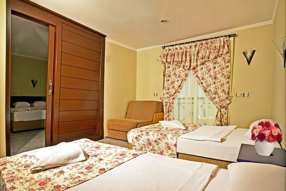 Ein Hotelzimmer mit zwei Betten, einem Sessel, einem Schreibtisch und einem Fenster mit floralem Vorhang.