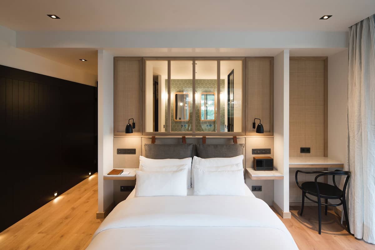 A modern hotel room with a large bed, bedside tables, a desk, and a chair.