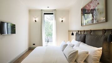 A bedroom with a large bed, two wall-mounted lights, a TV, and a window with curtains.