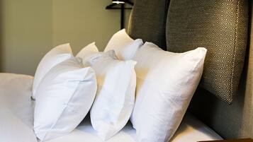 A neatly made bed with white pillows and a patterned pillow on a grey sofa.