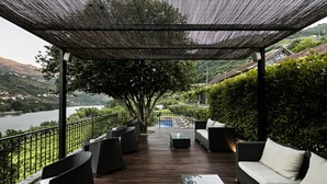 A covered outdoor deck with wicker furniture, a pool, and a view of a lake and hills. - Quinta de S. Bernardo Winery & Farmhouse (Mesão Frio)