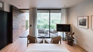 A bedroom with a large bed, two chairs, a TV, and a balcony with a view of greenery. - Quinta de S. Bernardo Winery & Farmhouse (Mesão Frio)