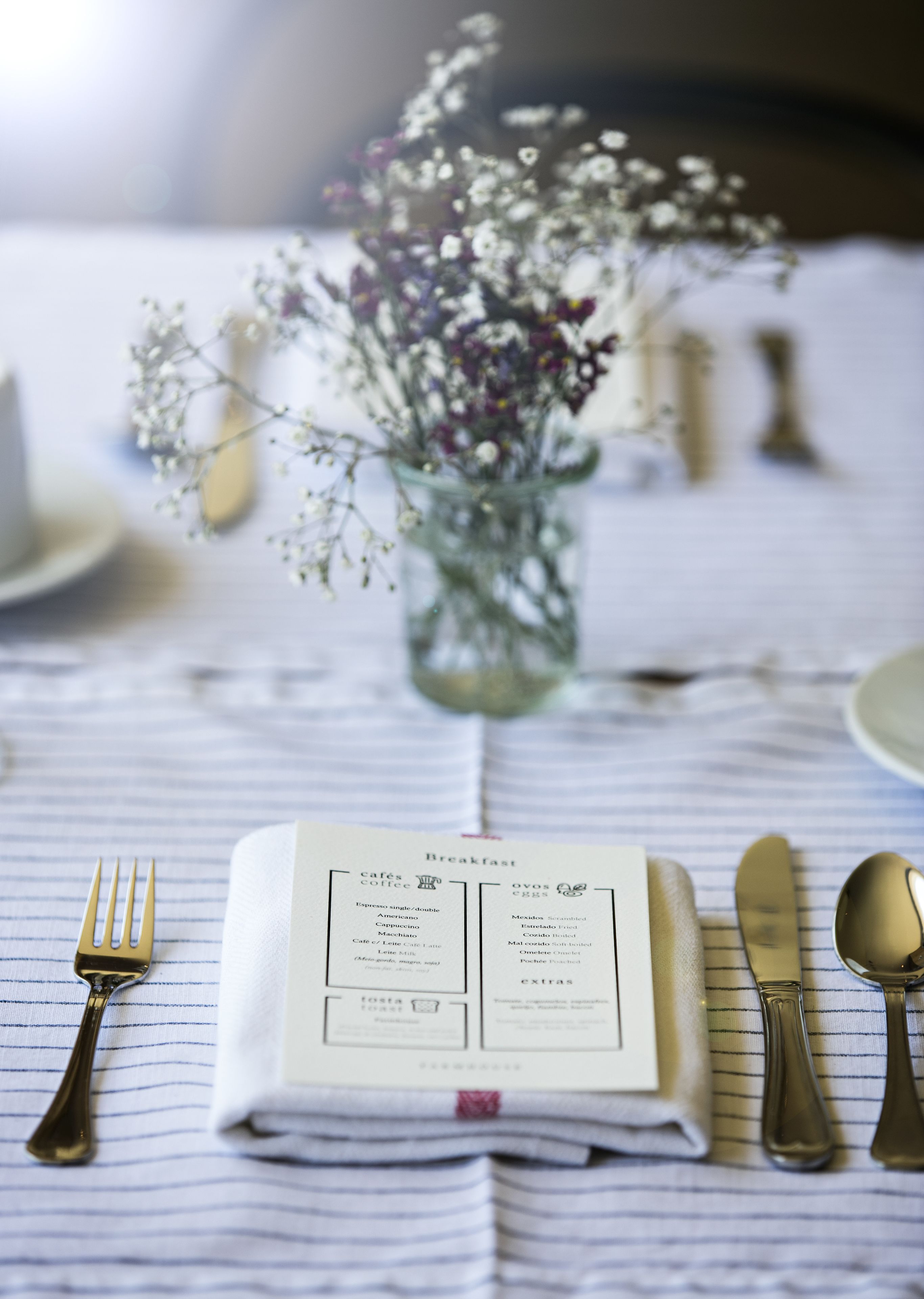 Una mesa de desayuno decorada con un menú, un jarrón de flores y cubiertos.