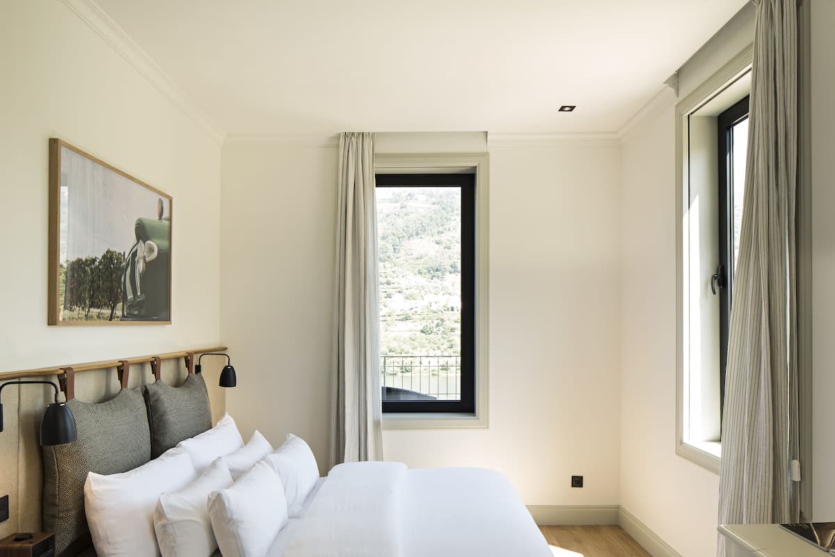 A bedroom with a large bed, a nightstand, a lamp, a chair, and a window with curtains.