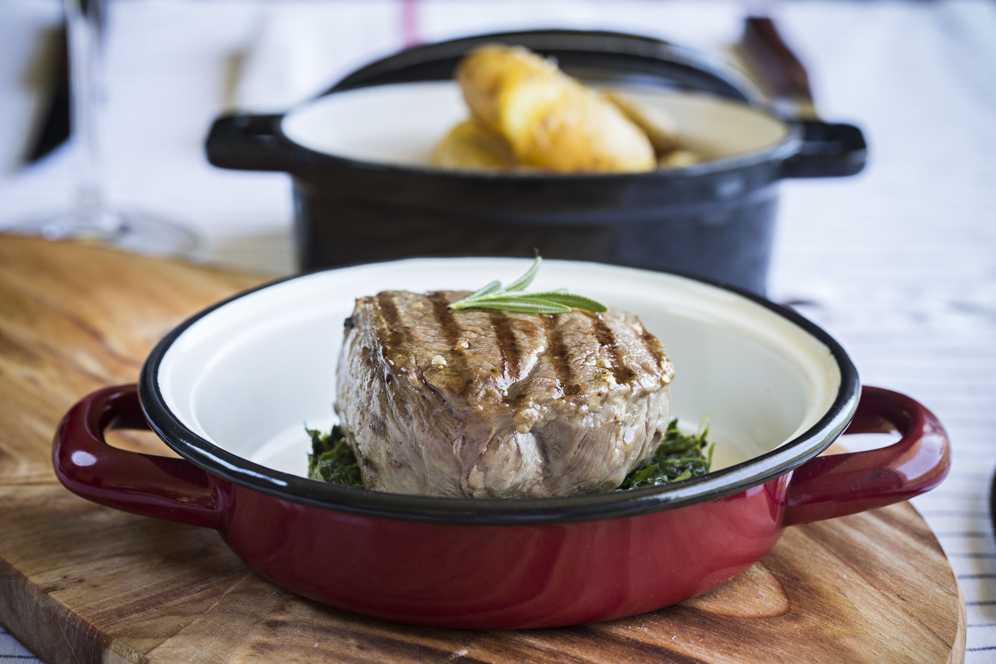 A red enameled cast iron pot with a roast on a wooden board.