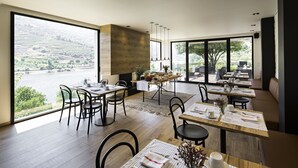 A modern dining area with large windows overlooking a scenic landscape. Tables are set with white tablecloths and neatly arranged cutlery. - Quinta de S. Bernardo Winery & Farmhouse (Mesão Frio)
