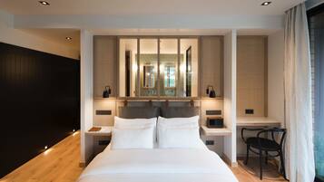 Quarto de hotel moderno com uma cama grande, mesas de cabeceira, escrivaninha e uma cadeira.