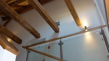 A wooden ceiling with exposed beams, a glass door with a metal frame, and a staircase with black tiles.