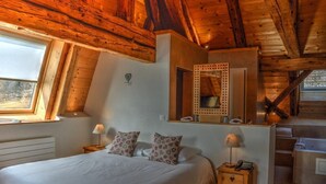 Une chambre avec un plafond en bois, un grand lit agrémenté d’oreillers à motifs, une table de chevet avec une lampe et un miroir au-dessus du lit.