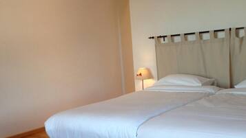 Une chambre d’hôtel avec un cadre de lit en bois, du linge de lit blanc, une table de chevet avec une lampe et un vase rempli de fleurs rouges posé sur une table en bois.