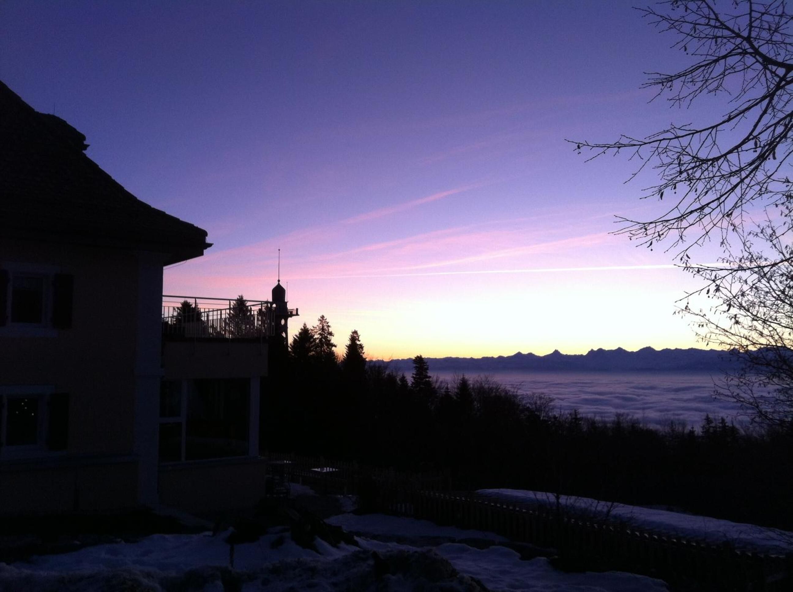 A house with a balcony overlooking a snowy landscape and distant mountains during twilight.