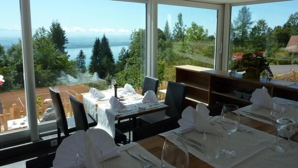 Un restaurant doté de grandes fenêtres offrant une vue panoramique sur des arbres et un plan d’eau.