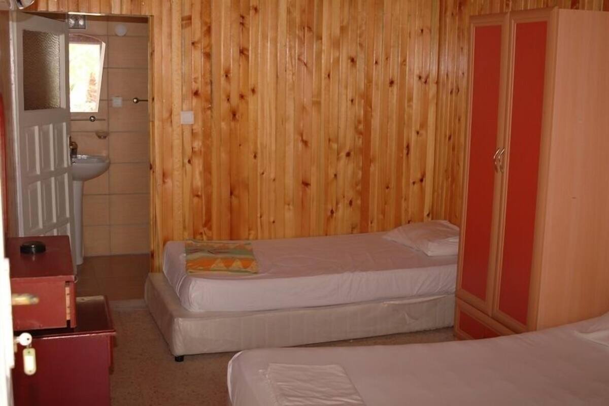 A room with two beds, a wooden wall, a red wardrobe, and a sink.