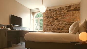 Un dormitorio con cama, escritorio, televisión y pared de piedra.