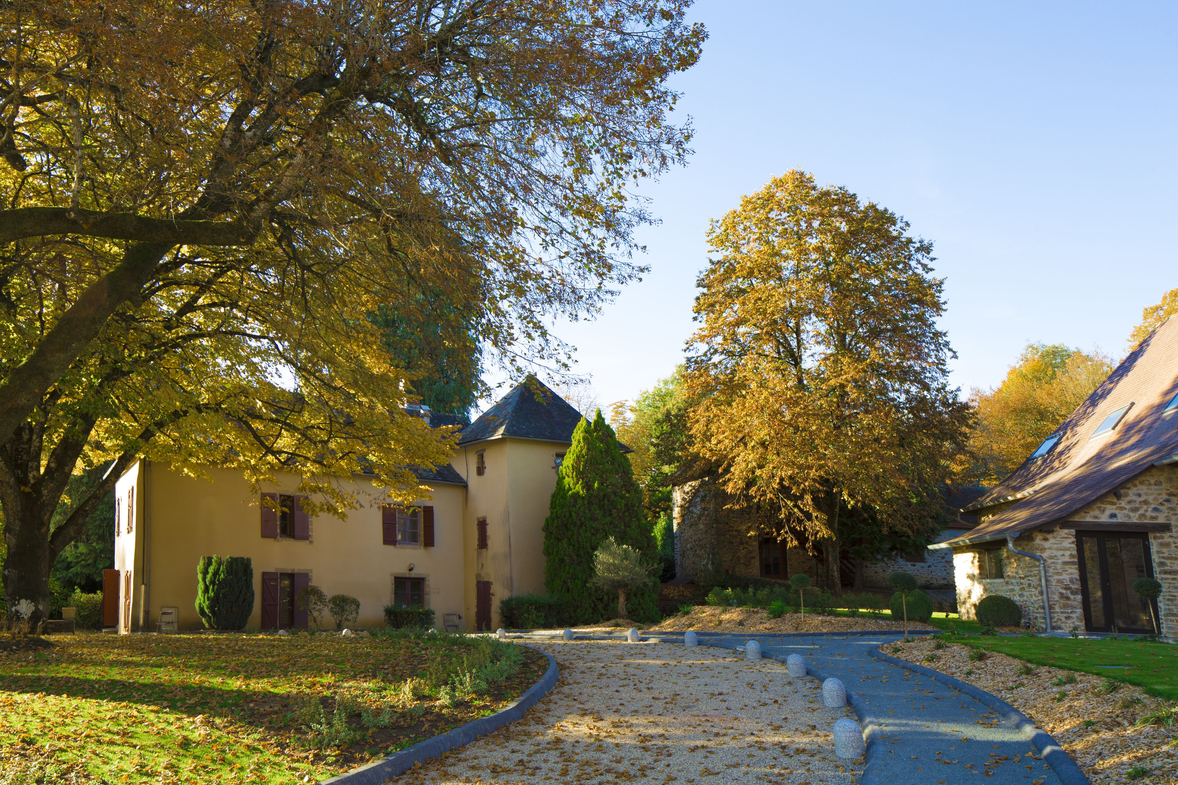 Ein gelbes Gebäude mit einer Steinaußenseite, einem Kiesweg und reifen Bäumen mit Herbstlaub.