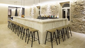 A bar area with a stone wall backdrop, a marble bar counter, and multiple bar stools. - Etoile de Pompadour (Beyssac)