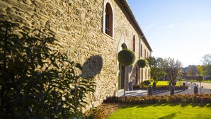 A stone building with arched windows and a well-maintained lawn with hedges. - Etoile de Pompadour (Beyssac)