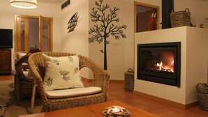 A cozy living room with a fireplace, wicker furniture, and a decorative tree wall decal. - Retiro do Bosque Country House (Alcanena)