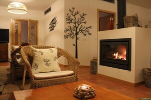 A cozy living room with a fireplace, wicker furniture, and a decorative tree wall decal.
