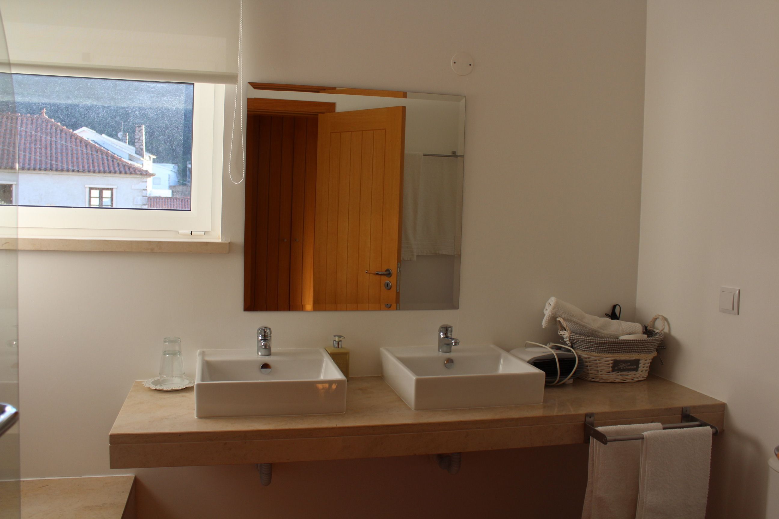 A bathroom with two sinks, a large mirror, and a window overlooking a house.