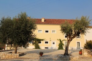 A two-story building with a red-tiled roof, a stone pathway, and potted plants.