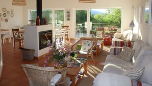 A spacious living room with a fireplace, comfortable seating, and large windows offering a view of the outdoors. - Retiro do Bosque Country House (Alcanena)