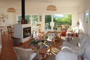 A spacious living room with a fireplace, comfortable seating, and large windows offering a view of the outdoors.