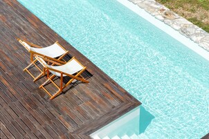 A wooden deck with two lounge chairs by a clear blue pool.